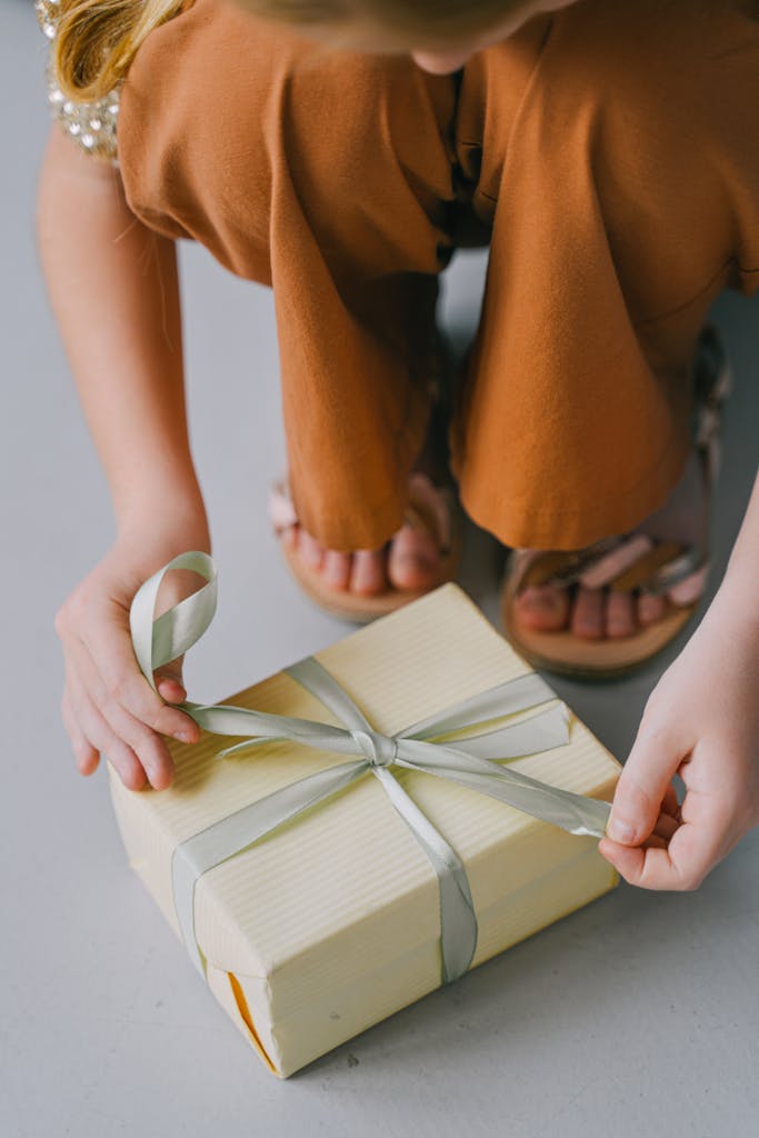 Close-up of a young girl tying a ribbon on a gift box, showcasing attention to detail and care.